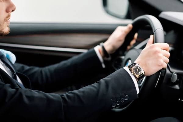 A driver in a dark suit at the wheel of a black car