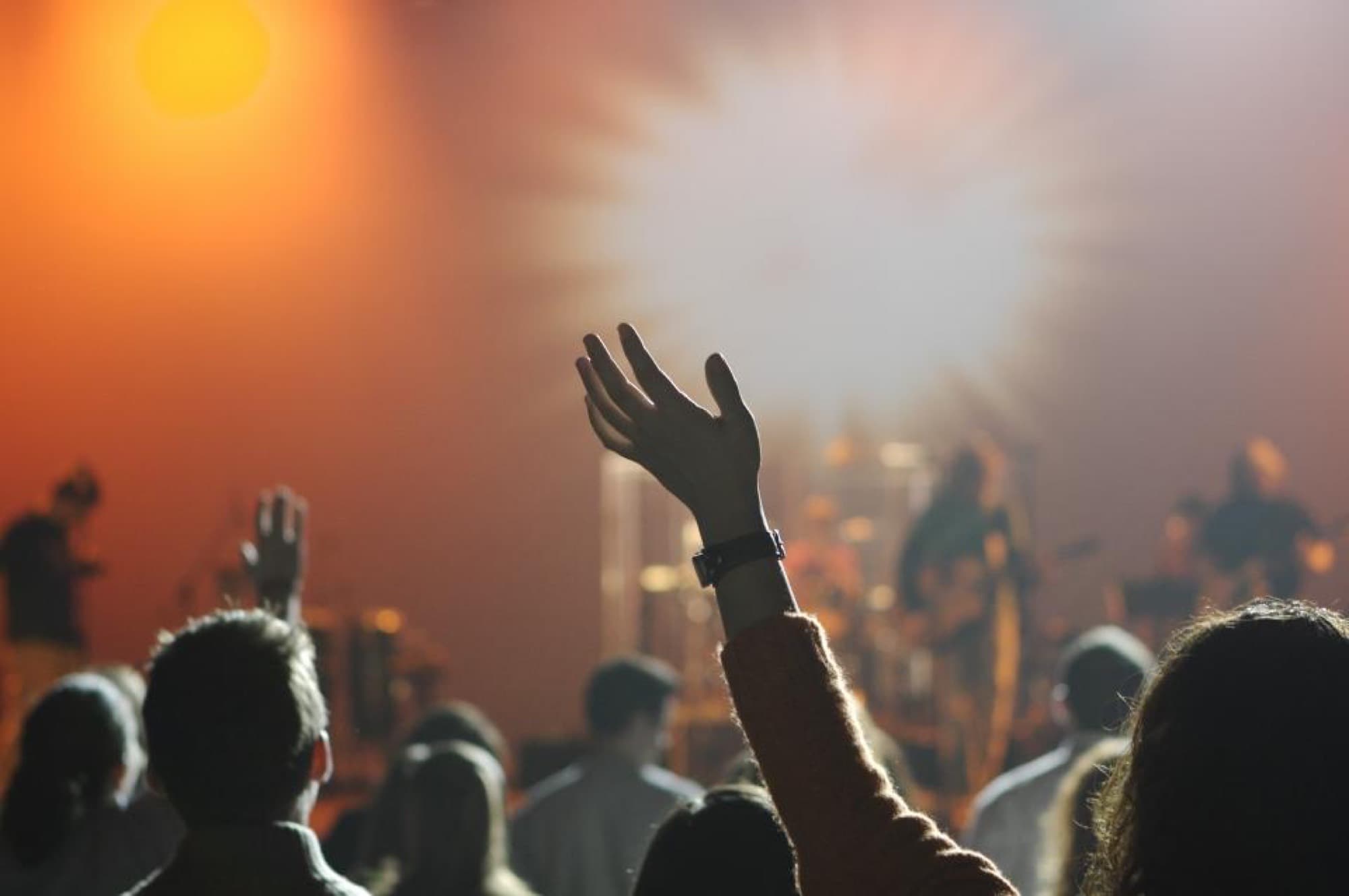 A crowd with hands raised in front of a lit concert stage