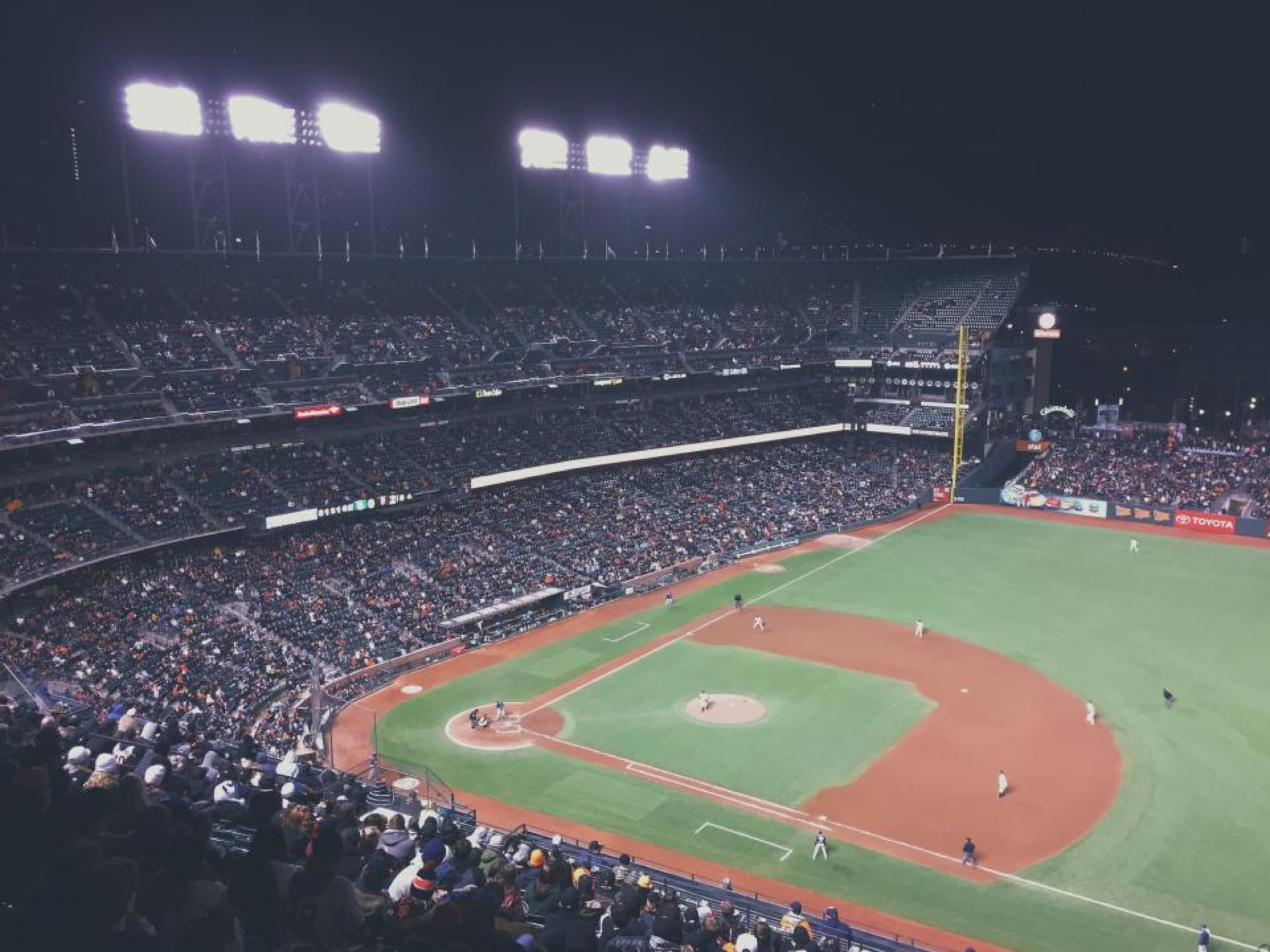 A floodlit ballpark at night with a full crowd